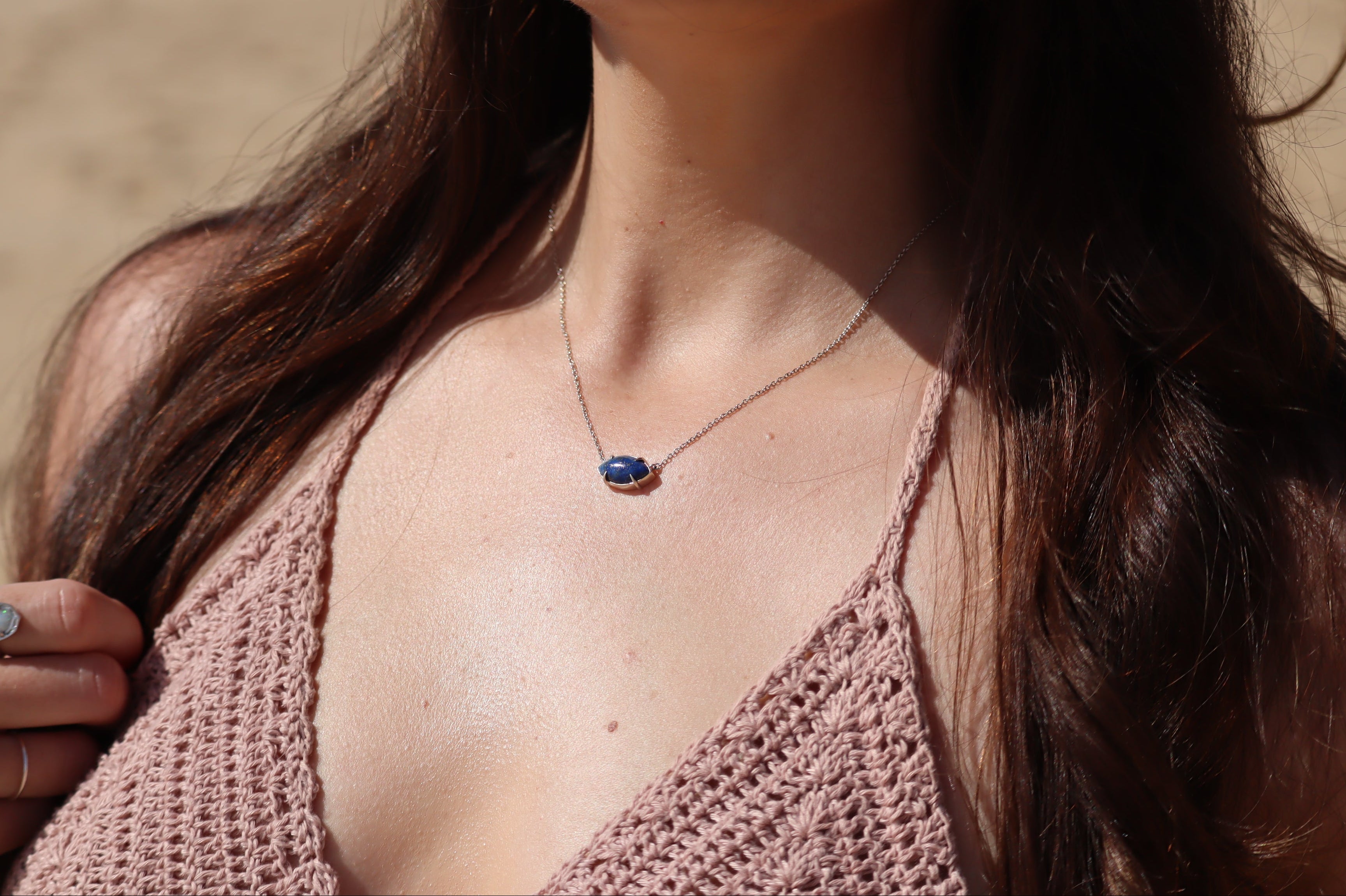 Woman wearing a silver necklace with a marquise shape, blue lapis lazuli pendant in a beach setting