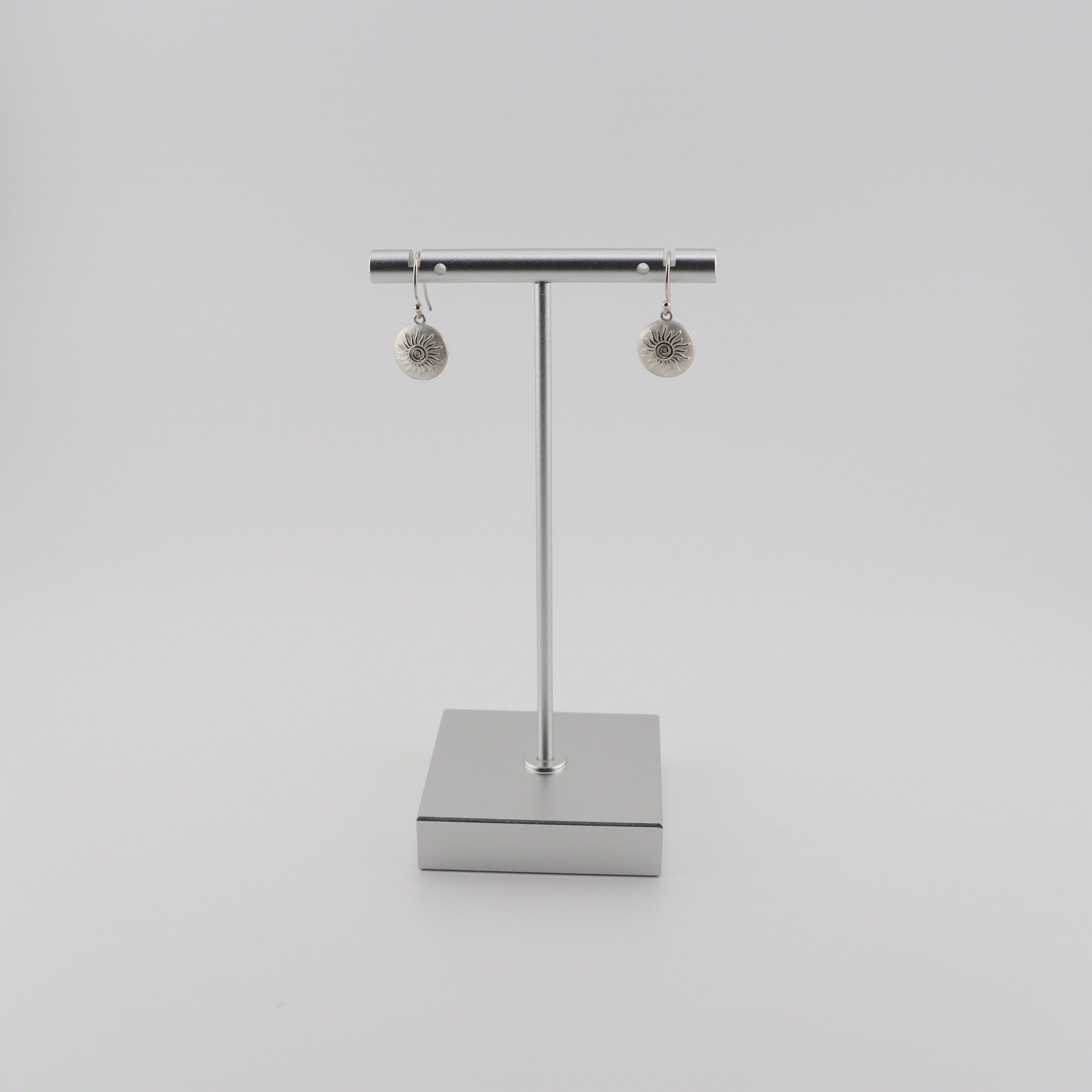 Silver shepherd hook earrings with sun detail on a stand against a white background