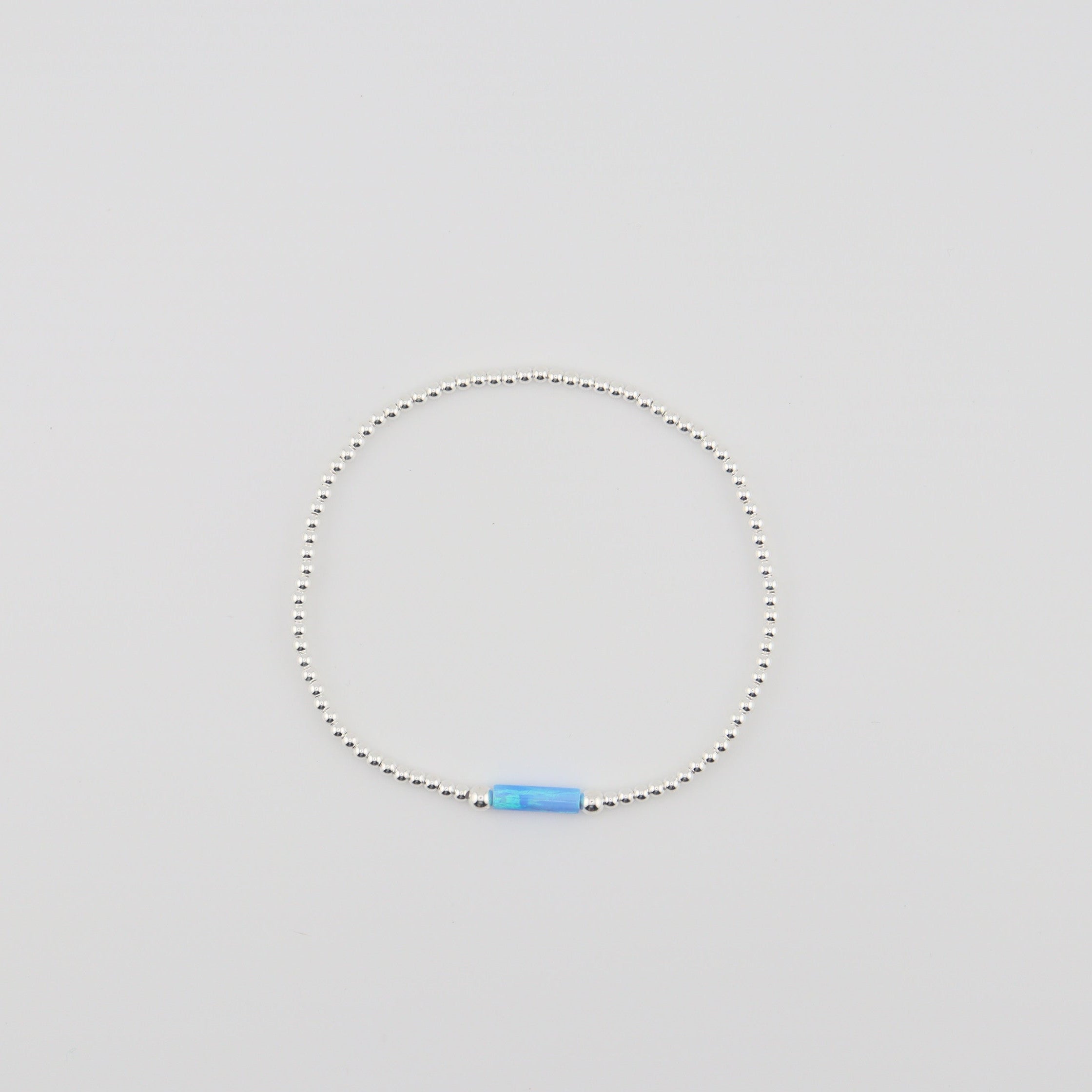 Silver beaded bracelet with a blue accent bead on a light gray background