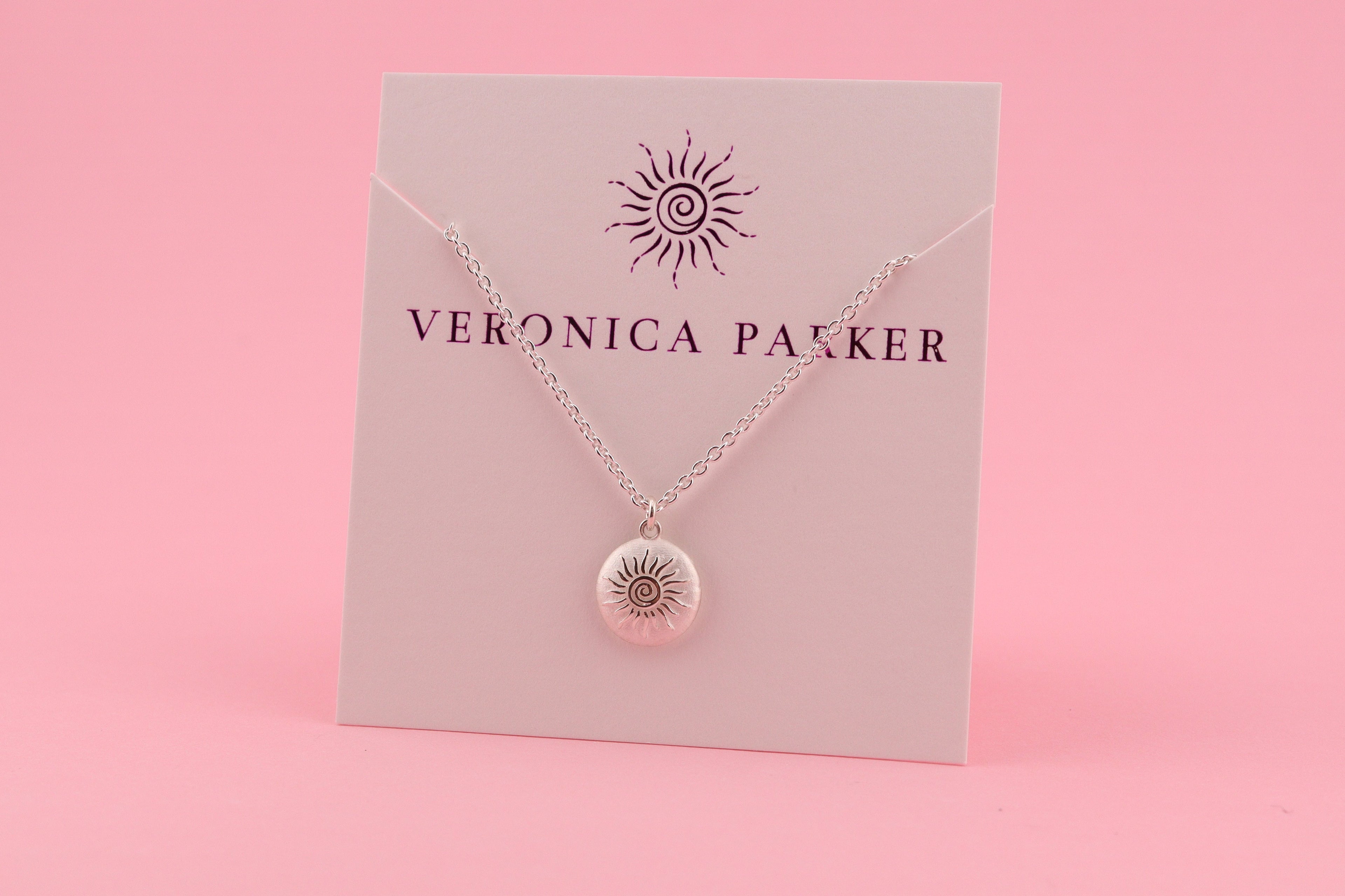 Silver necklace with a pendant on a pink card with 'Veronica Pakker' branding against a pink background
