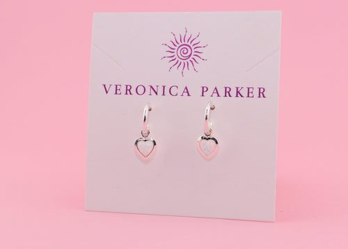 Heart-shaped earrings with white lab-created opals on a Veronica Parker card with a pink background