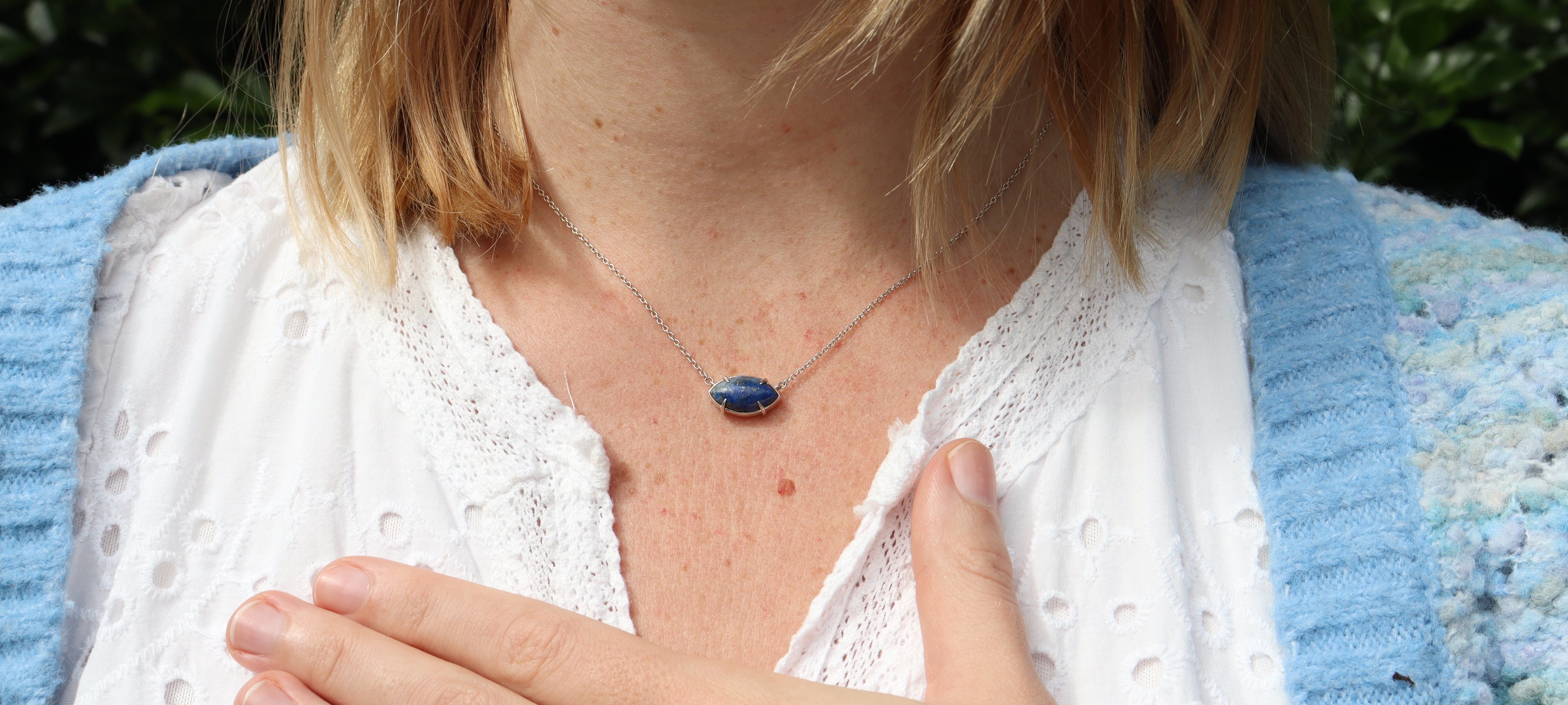 Blue lapis lazuli marquise necklace on silver chain modeled by blonde girl wearing white dress with blue cardigan