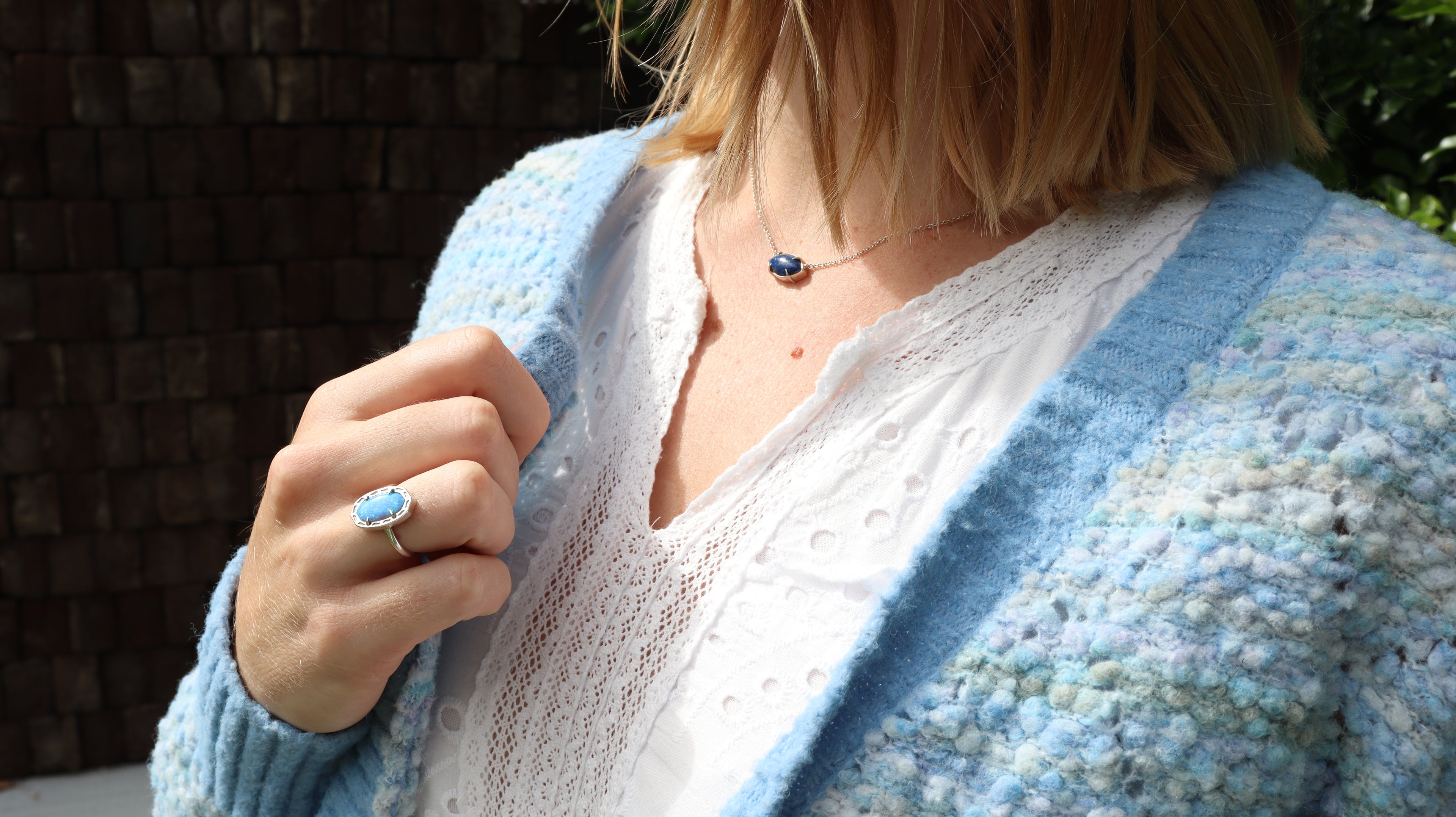 Blue lapis lazuli marquise necklace on silver chain modeled by blonde girl wearing white dress with blue cardigan